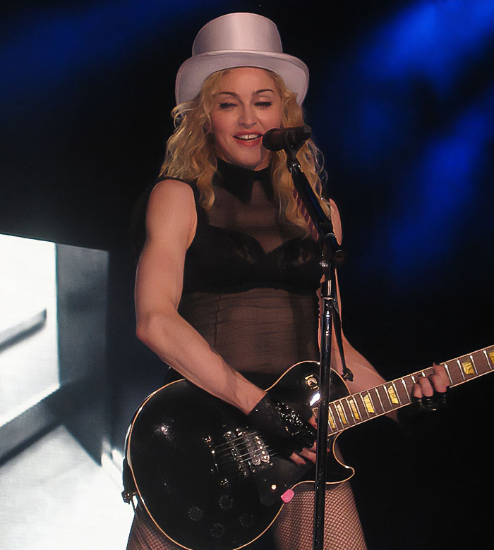 Madonna performing on stage wearing a white hat and playing guitar, fans notice the famous gap missing from her face