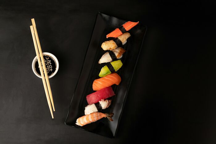 Assorted sushi pieces on a black plate with soy sauce and chopsticks, illustrating common foods that spoil quickly.