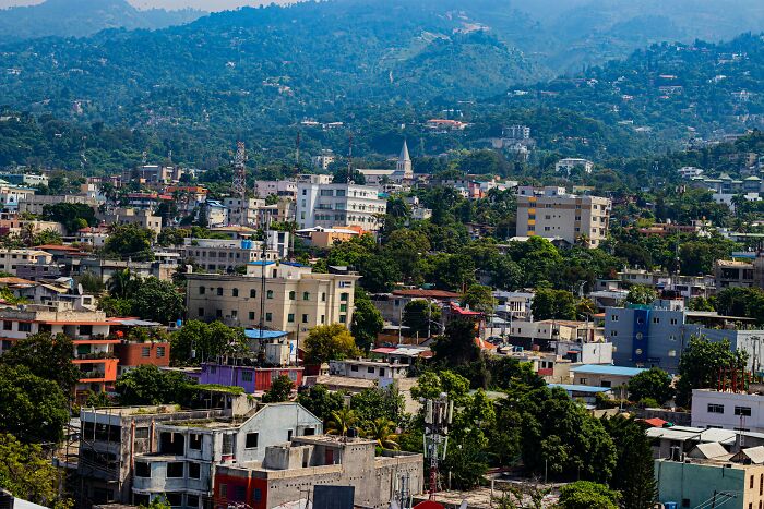 A dense cityscape with mixed residential and commercial buildings surrounded by green hills under a clear sky.