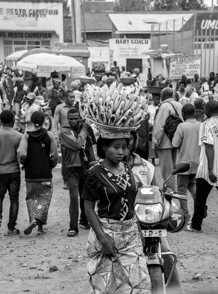 Woman balancing bananas on her head in a busy market, illustrating a major event happening today not covered by mainstream media.