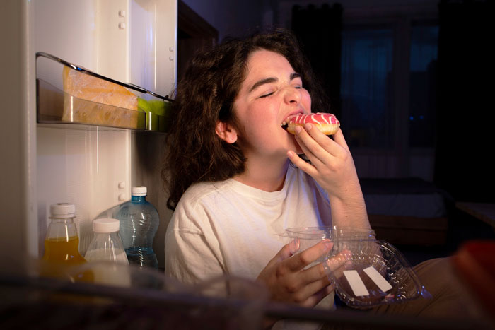 Teen girl eating a doughnut from the fridge, illustrating teen kids paying for their own junk food at home. Teen girl eating a doughnut from the fridge, illustrating teen kids paying for their own junk food at home.
