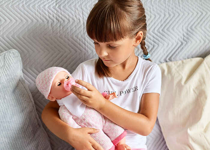 Young girl playing with a baby doll, reflecting pregnancy-obsessed child receiving a weird gift from MIL.