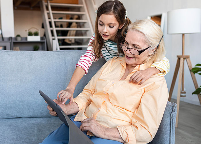 Young girl with grandmother on sofa using a tablet, illustrating mom furious over MIL's weird gift to pregnancy-obsessed child.