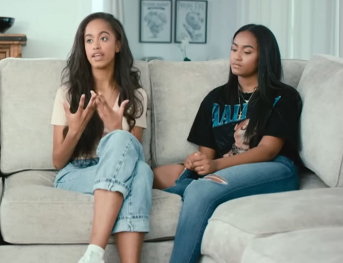 Sasha Obama and Malia sitting on a couch, with Sasha showing off figure while discussing family topics. Sasha Obama and Malia sitting on a couch, with Sasha showing off figure while discussing family topics.