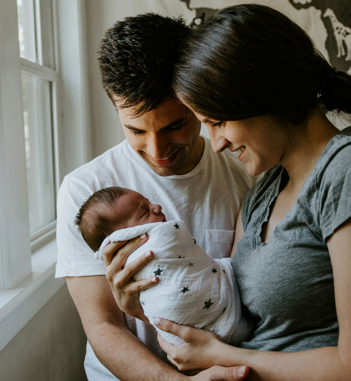 Young couple holding newborn baby, capturing a tender moment after a traumatic birth experience at home.