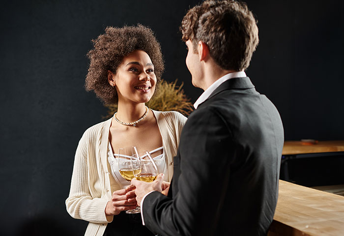 A woman and man holding wine glasses, smiling and talking, illustrating a fake twin brother confession scenario. A woman and man holding wine glasses, smiling and talking, illustrating a fake twin brother confession scenario.