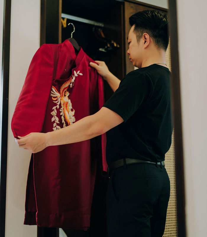 Man housesitting, holding a red embroidered jacket, trying on clothing for thrills inside a home closet.