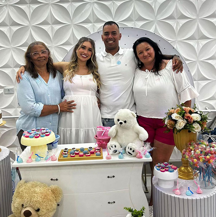 Family celebrating baby's gender reveal with cupcakes, teddy bears, and flowers in a decorated room.