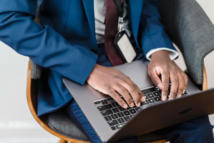 Manager typing on laptop, wearing blue suit and an ID badge, representing workplace conflict and baseless claims scenario.