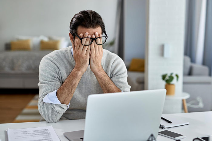 Stressed engineer in glasses sitting at desk with laptop, covering face, suspecting file deletion issue in office setting.