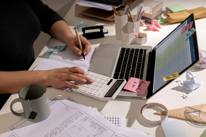 Person using a calculator and laptop with spreadsheets and notes, suggesting manager thinks engineer lies about deleting file.