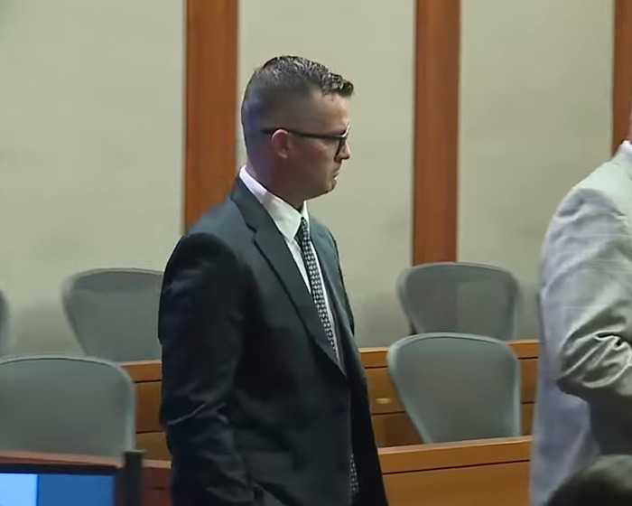 Man in glasses and suit standing in courtroom during marriage revelation case involving toddler left in hot car. Man in glasses and suit standing in courtroom during marriage revelation case involving toddler left in hot car.