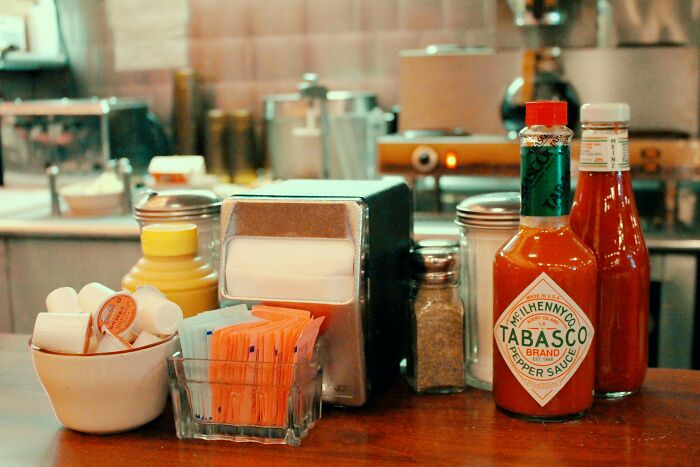 Condiment bottles and sweetener packets on a diner counter with folks revealing hilarious girlfriend secrets.