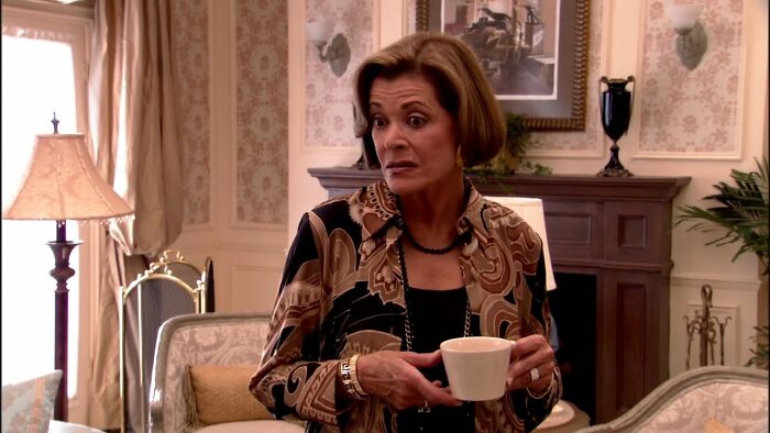 Woman in patterned blouse holding a coffee cup with a shocked expression, illustrating jaw-dropping moments of online shaming.