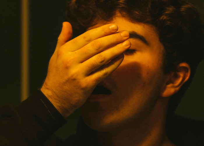 Young medical worker covering face with hand, pretending to stay calm while seeing something unbelievable.