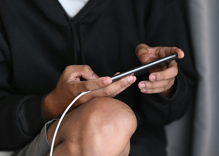 Person wearing a black hoodie holding a smartphone with a charging cable, illustrating medical workers pretending to be calm.