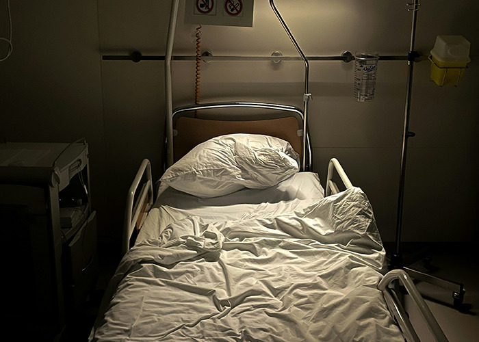 Empty hospital bed with medical equipment in dim light, capturing medical workers pretending to be calm atmosphere.