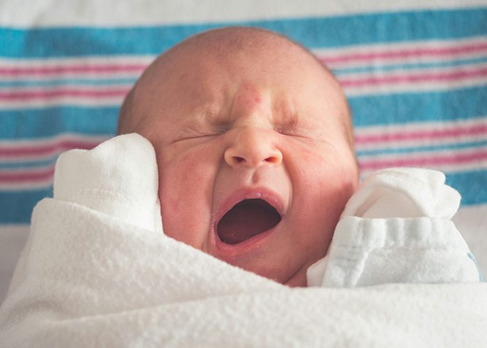 Newborn baby wrapped in a blanket yawning, a common sight for medical workers staying calm in surprising moments.