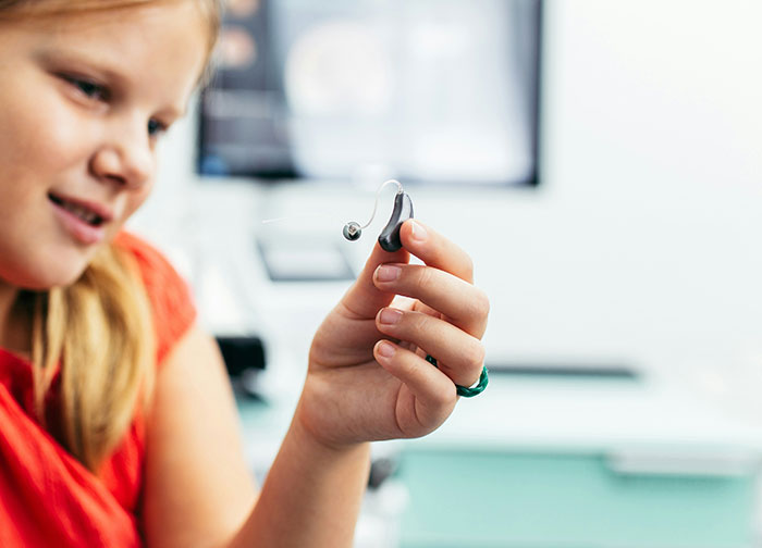 Young girl examining a small hearing aid device, highlighting patient experience and hurtful things doctors said and did.