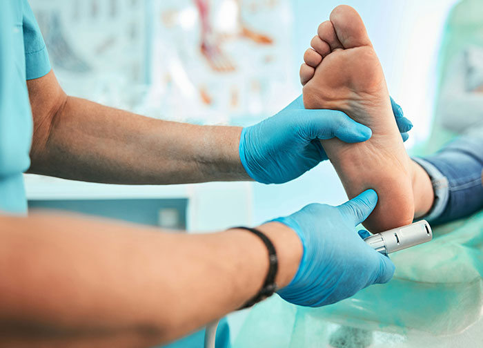 Doctor wearing blue gloves examining a patient’s foot during a medical checkup in a clinical setting.