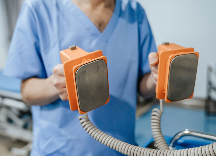Medical professional in scrubs holding defibrillator paddles showing powerful medical equipment used by doctors