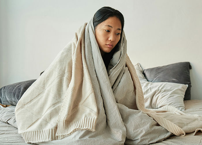 Young woman wrapped in a blanket looking sad, reflecting hurtful things doctors said that made patients want to change doctors.