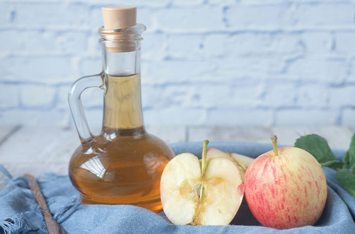 Bottle of apple cider vinegar and fresh apples on a cloth, illustrating healthy foods to skip as shared by dentists and doctors.