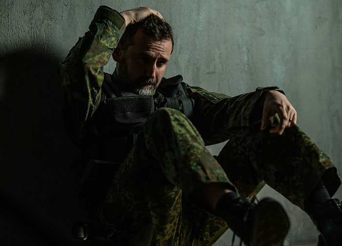 Worried man in military uniform sitting against wall, reflecting on hurtful things doctors said and patient trust issues.