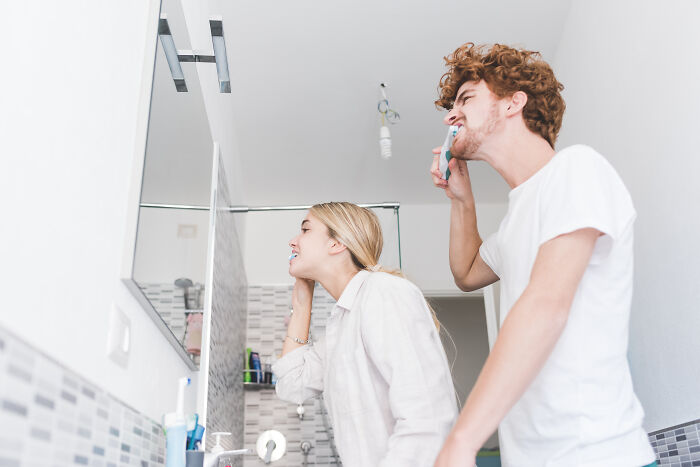 Young man and woman brushing teeth in bathroom, illustrating mundane things that make people sick and hygiene risks.