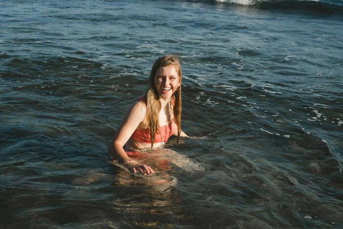 Young woman in a red swimsuit sitting in ocean water, representing mundane things that can make people sick.