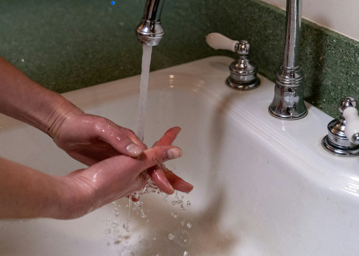 Hands of a medical field employee washing under running water in a sink to maintain hygiene and safety standards.