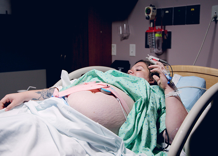 Pregnant woman in hospital bed monitored by medical field employees during labor to ensure safe delivery.