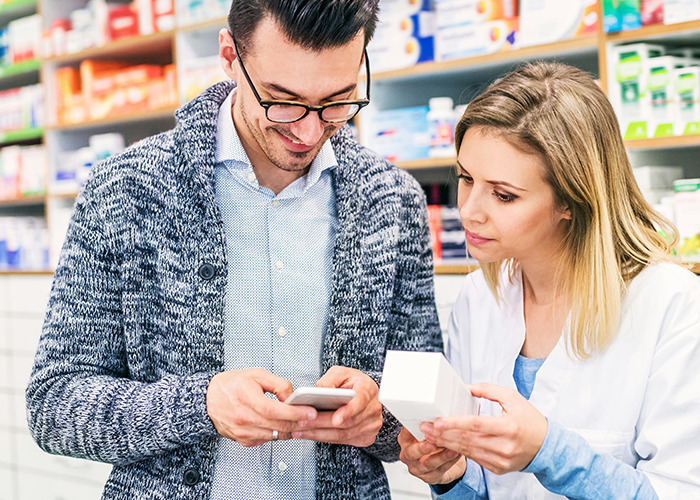 Medical field employee in a pharmacy explaining medication details to a customer in a well-stocked medical environment