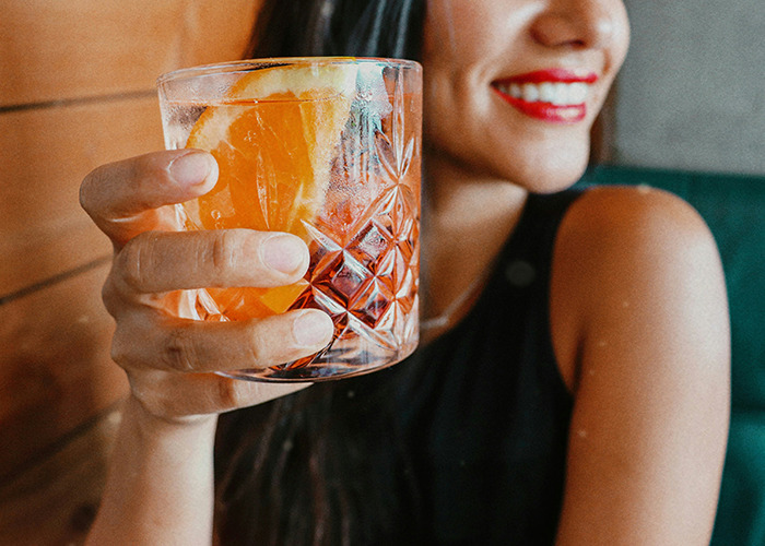 Woman in a black top holding a glass with orange slice, representing insights from medical field employees.
