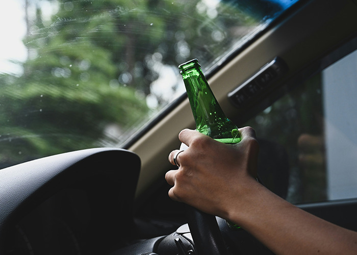 Person holding a green bottle while driving a car, illustrating risky behavior medical field employees would never do.