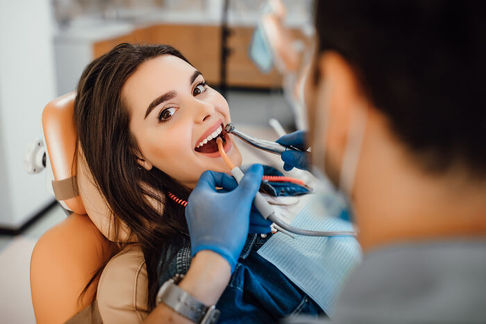 Young woman at dental checkup, dentist examining her teeth, highlighting unique body features discussion online.