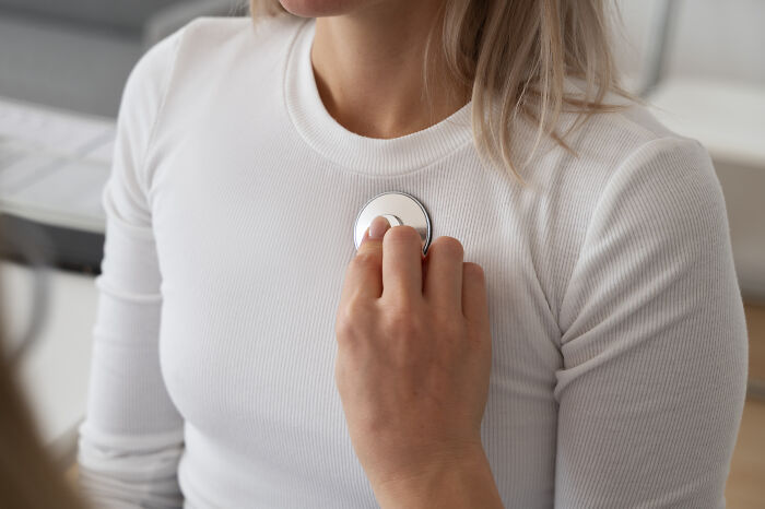 Person in a white shirt having their unique body feature checked with a stethoscope by a medical professional
