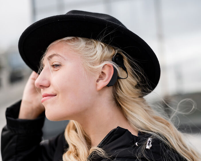 Young woman with unique body features wearing a black hat and a hearing aid outdoors in natural light