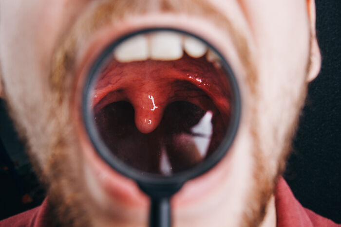 Close-up of a person’s open mouth showing unique body features examined with a magnifying glass.