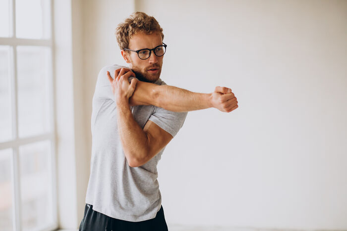 Man with glasses stretching his arm indoors, illustrating unique body features discussed by netizens in a casual setting.