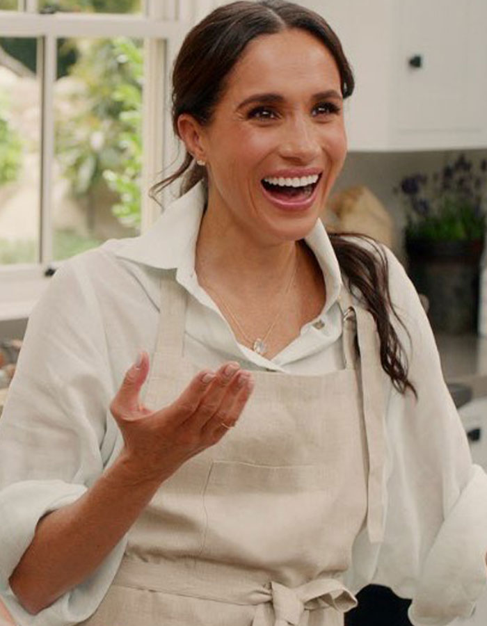 Meghan smiling in a kitchen wearing an apron as Harry&rsquo;s crisis raises mental health concerns in the royal family.