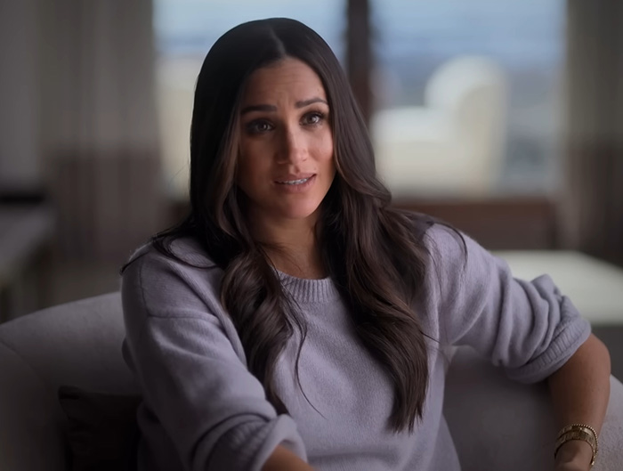 Meghan Markle speaking indoors wearing a gray sweater, allegedly berating her wedding caterer during an intense moment.