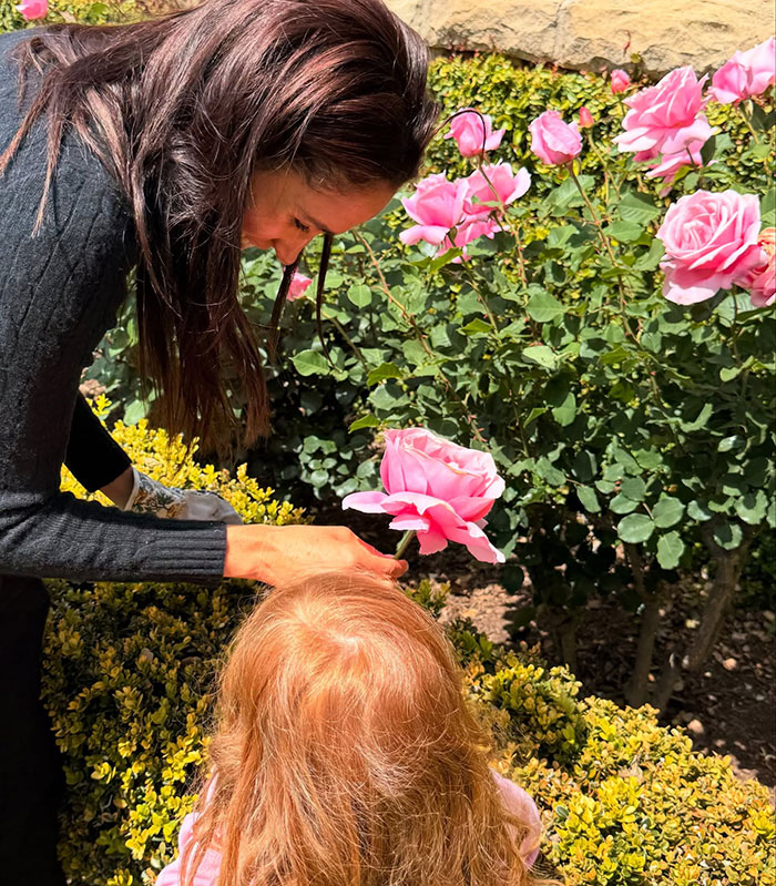 Meghan Markle tending roses outdoors with 3-year-old Lilibet, featuring a close moment in a garden with pink flowers. Meghan Markle tending roses outdoors with 3-year-old Lilibet, featuring a close moment in a garden with pink flowers.