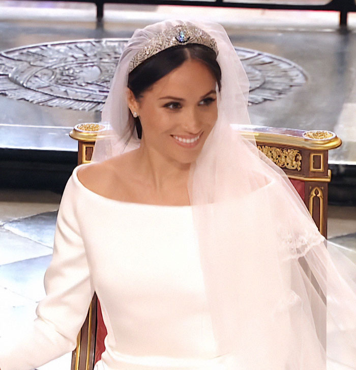 Meghan Markle in a white wedding dress and tiara during royal ceremony, facing criticism for not mentioning Prince Harry.