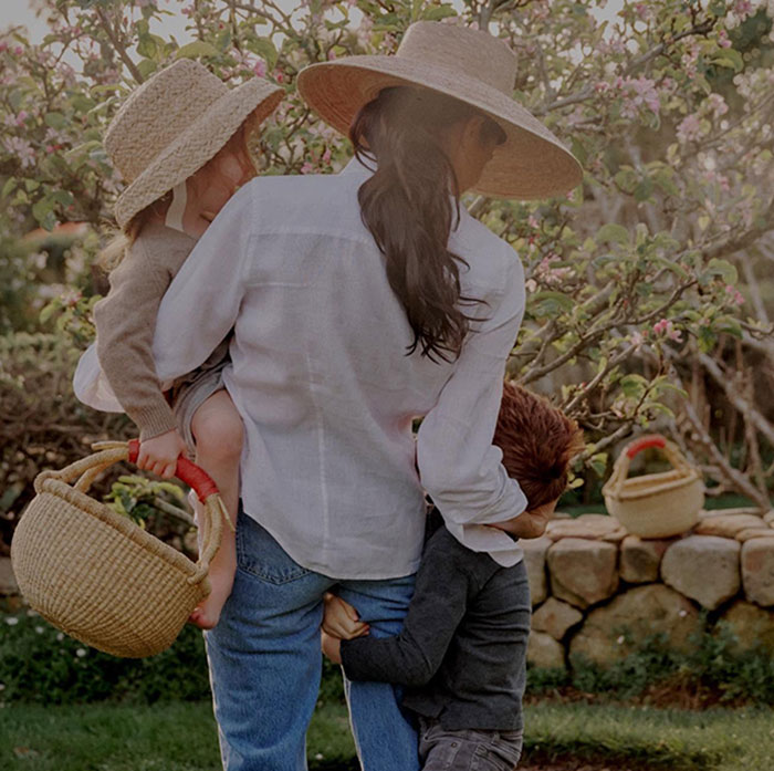 Meghan Markle holding children outdoors in a garden setting, highlighting a beekeeping moment with 3-year-old Lilibet. Meghan Markle holding children outdoors in a garden setting, highlighting a beekeeping moment with 3-year-old Lilibet.