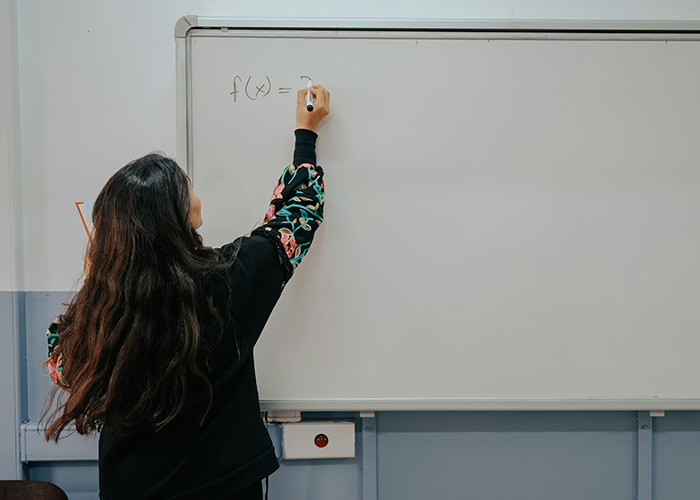 Woman with long hair writing a math function on a whiteboard, illustrating moments that would be outrageous if genders were reversed