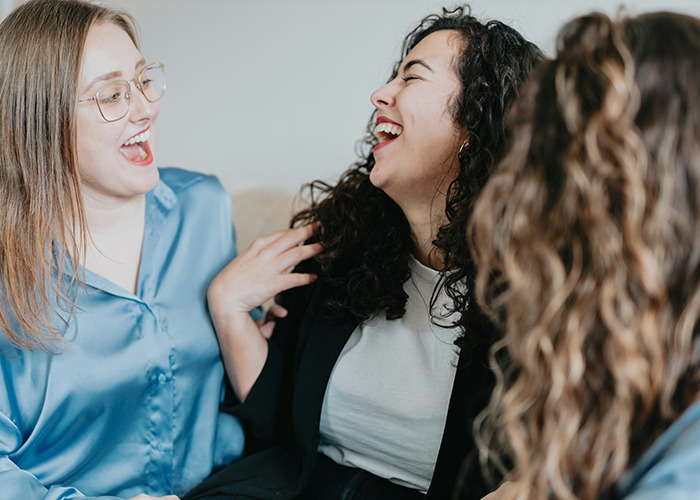 Three women laughing and sharing stories, illustrating moments that would be outrageous if the genders were reversed.