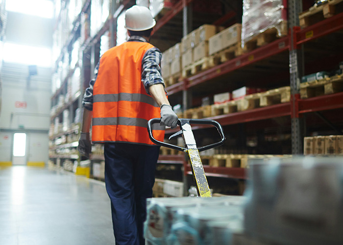 Man in safety vest and helmet operating pallet jack in warehouse, illustrating moments men share that seem outrageous if reversed.