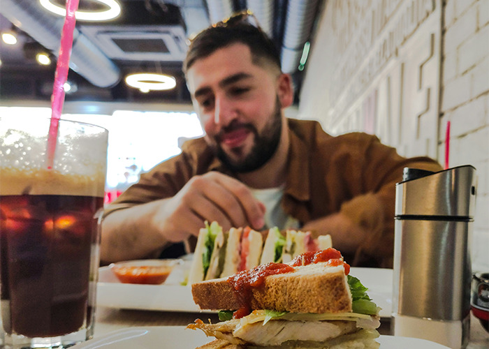 Man enjoying a sandwich and drink at a cafe, illustrating moments shared by men that challenge gender norms.