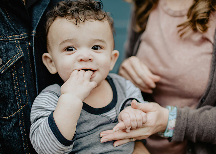 A young child with fingers in mouth being held by adults, illustrating moments shared by men and gender perspectives.
